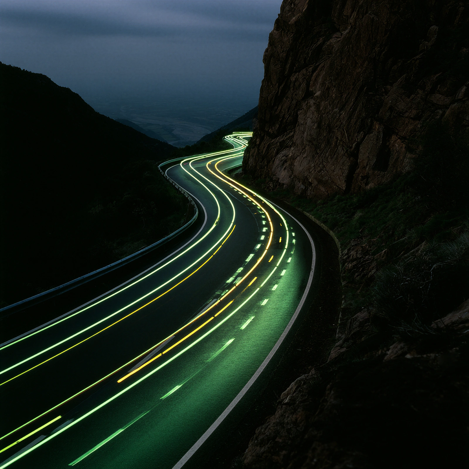 Light trails of vehicles on a winding mountain road at night.